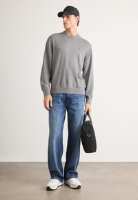Maglione grigio a maglia, jeans blu, sneakers bianche e una borsa nera. Outfit casual con scollo rotondo e polsini a costine.