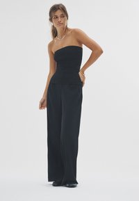 Zwarte strapless top met een aansluitend lijfje, gecombineerd met zwarte broek met wijdvallende pijpen. Gladde textuur, minimalistisch ontwerp en subtiele afwerking.