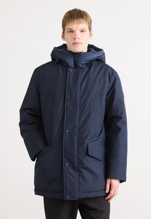 Navy blue insulated parka with a hood, featuring a zip front and snap buttons, large side pockets, and a textured fabric finish.