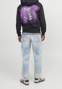 Felpa nera con un design grafico viola che presenta uno scorpione e stelle. Abbinata a jeans chiari strappati e sneakers grigie.