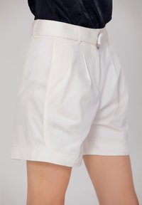 Shorts plissés blancs avec une finition en tissu lisse et une taille ajustée, dotés d'un fermoir à l'avant et de poches latérales.