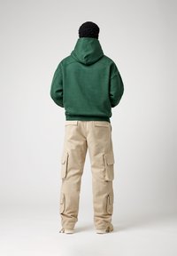 Groene hoodie met een relaxte pasvorm, gecombineerd met beige cargobroek met zijzakken. Eenvoudig ontwerp, soepele textuur en comfortabele uitstraling.
