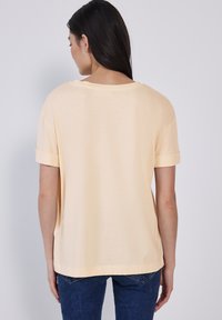 Camiseta corta de manga corta de color amarillo claro con un corte relajado y mangas enrolladas. Textura suave, escote redondeado y dobladillo recto.