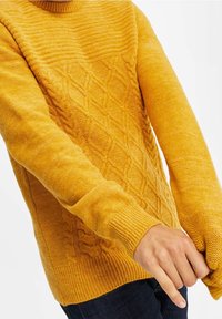 Stickad tröja i en djup gul färg med en strukturerad kabelstickningsdesign på kroppen och ribbade muddarna. Långärmad; avslappnad passform.