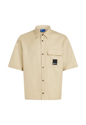 Rövid ujjú ing bézs színű pamutszövetből, mellkasi zsebbel, fekete gombos záródással és címke részlettel a zseben. Sima textúra.