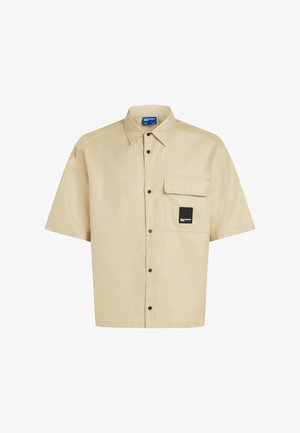 Kortärmelig overhemd van beige katoen met een borstzak, zwarte knoopsluiting en merkembleem op de zak. Gladde textuur.