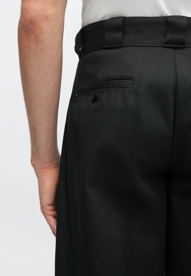 Sorte bukser lavet af glat stof, med en standard talje, en enkelt baglomme med knap og en skræddersyet pasform.
