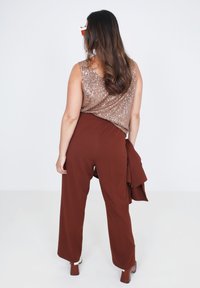 Pailletten top in roségoud gecombineerd met brede, bruine broeken. De outfit heeft zachte texturen en een gelaagd ontwerp met vloeiende stof.