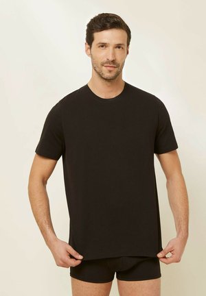 Tricou din bumbac negru cu guler clasic rotund și mâneci scurte, având o croială lejeră și un design simplu, asortat cu șorturi boxer negre.