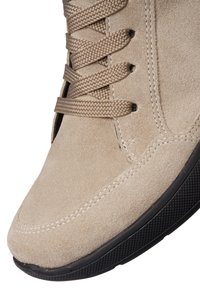 Zapatilla alta de ante beige con superficie texturizada, punta redonda, suela de goma negra y cordones a tono. Detalles de costura visibles en la parte superior.