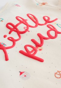 Tissu en coton avec une base crème ornée de motifs ludiques. Lettres rouges audacieuses et texturées épelant "little pud", entourées de motifs festifs.