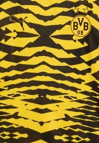 Maglia con marchio Puma realizzata in un brillante tessuto giallo con un motivo a zigzag nero, include un logo circolare del club e due stelle dorate sopra di esso.