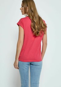 Kortärmad, korallfärgad T-shirt med avslappnad passform, med en mjuk textur och rundad halsringning, tillsammans med ljusblå tajta jeans.