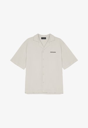 Harmaa lyhythihainen nappipaita, jossa on pehmeä tekstuuri ja musta "PEGADOR" -logo vasemmalla rintataskussa. Klassinen kaulustyyny.