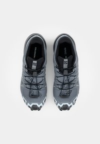 Chaussures de sport grises avec un dessus texturé, ornées de lacets noirs, d'éléments de design angulaires et d'une semelle extérieure gris clair avec un motif de bande de roulement prononcé.