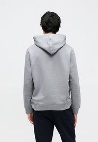 Hallikas kapuutsiga dressipluus, millel on sile tekstuur, soonikkäised ja soonikservad. Omadusteks on lõdvestunud istuvus ja esiküljel kängurutasku.