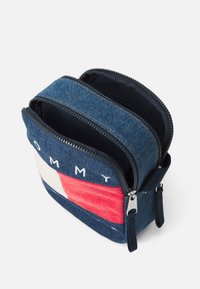 Denim crossover-veske med røde og hvite striper, glidelåslukking og brodert logo. Har en kompakt rektangulær form og to rom.