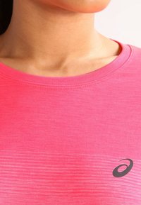 Vaaleanpunainen lyhythihainen urheiluponcho, joka on valmistettu sileästä ja kevyestä kankaasta. Sisältää hienovaraisen liukuvärjäyskuvion ja mustan logon rinnassa.