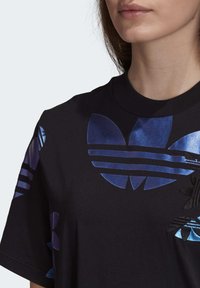 Svart t-shirt med kort ärm, utsmyckad med glansiga blåa och svarta adidas trefoil-logotypdetaljer samt ränder på axlarna. Slät tygtextur.