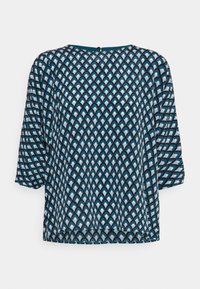 Haut ample à manches courtes bleu et blanc, présentant un motif géométrique en écailles, avec un col rond et une fermeture à boutons à l'arrière.