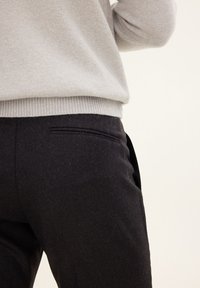 Gray sweater paired with black wool trousers featuring a smooth texture, side pockets, and a subtle pattern on the fabric.