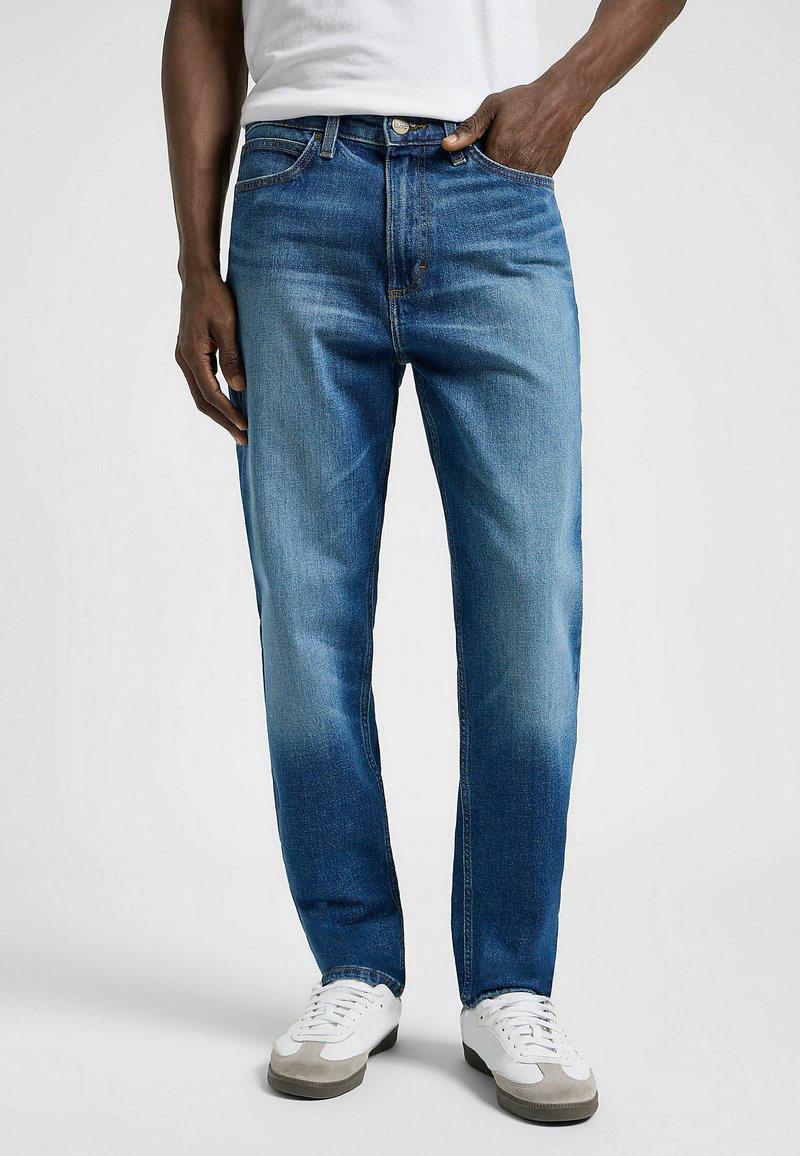 Jeans de mezclilla azul con un diseño de pierna recta, que presentan desvanecimiento cerca del muslo, estilo clásico de cinco bolsillos y cierre de botón de metal.