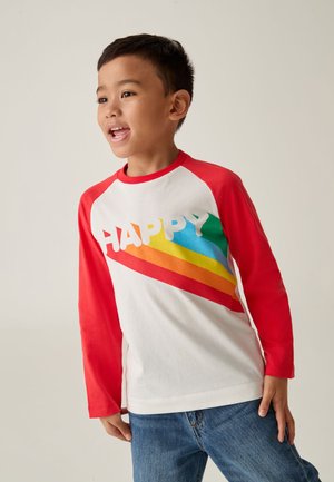 Camisa blanca de manga larga con mangas raglán rojas, que presenta la palabra "HAPPY" en letras gruesas y un diseño de franjas diagonales de arcoíris.