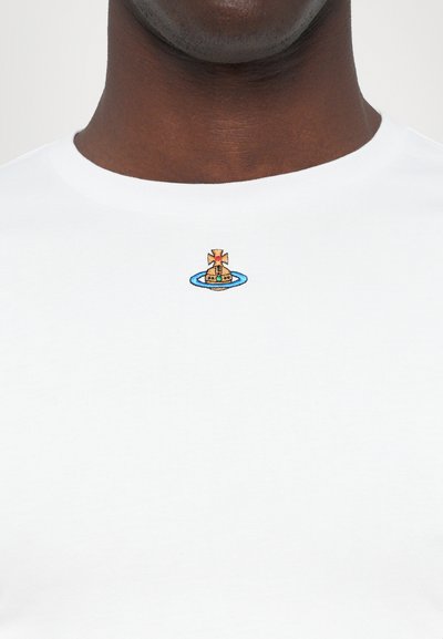 Vit bomullströja med rund halsringning, prydd med en liten broderad design av en båt och ett kors i färgerna blå, guld och röd.