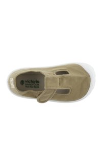 Scarpa di tela kaki con suola in gomma bianca, dotata di una fascia in Velcro e dettagli ritagliati per la ventilazione. L'interno mostra il logo del marchio.