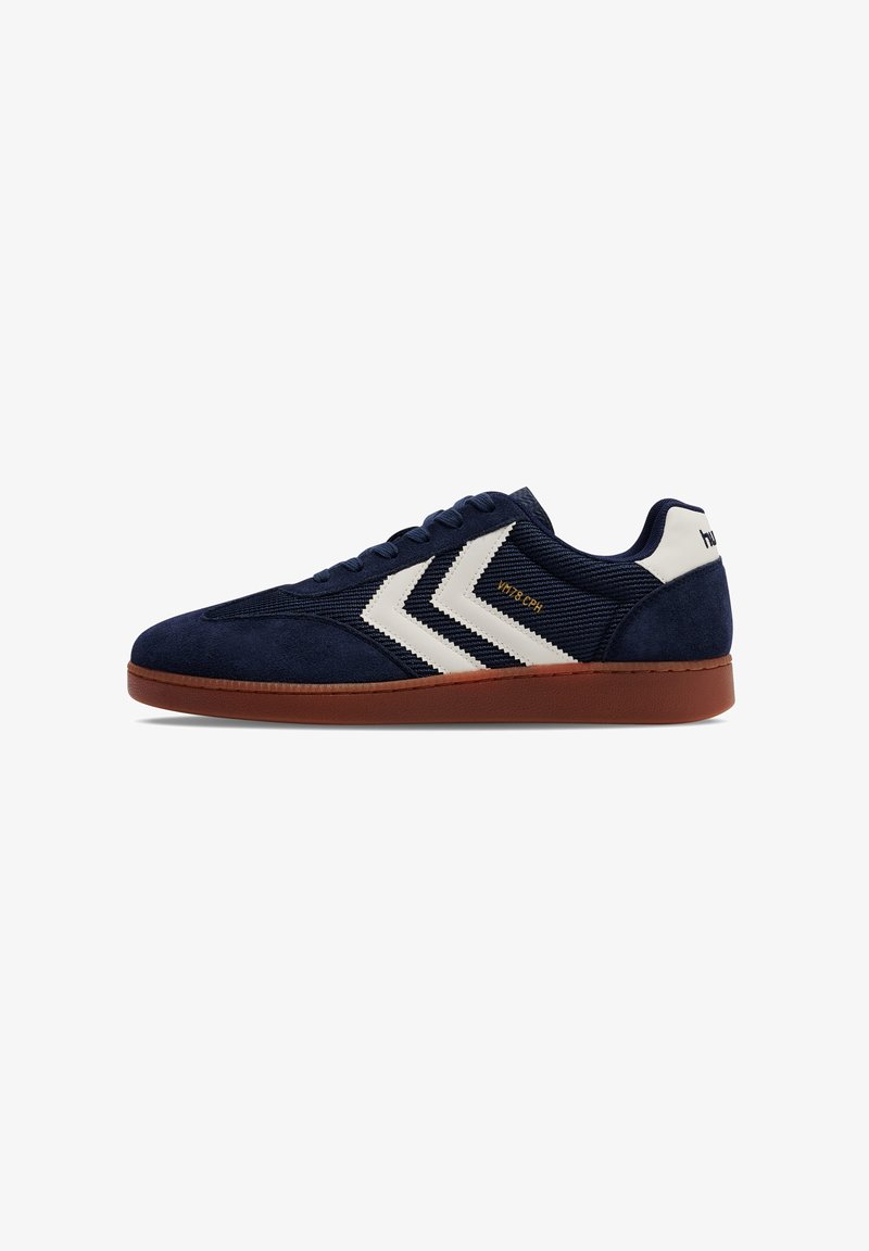 Navy suede sneakers with white chevron design, textured fabric upper, round toe, and brown rubber sole. Features stitched detailing.
