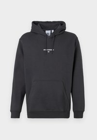 Melnā kapucīna džemperis ar kangaroo kabatu, aukliņu kapuci un baltiem uzdrukātiem vārdiem "ADIDAS ORIGINALS" uz krūšu daļas. Gluda auduma tekstūra.