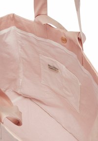 Sac tote en coton rose avec une texture lisse, doté d'une petite poche intérieure avec une étiquette. Fermé par un bouton doré.