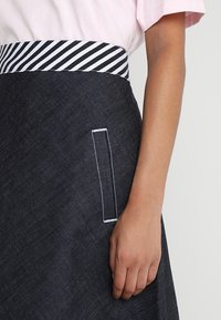 Gonna di denim con una vita a righe bianche e nere, dotata di una tasca laterale con cuciture bianche e un tessuto liscio e testurizzato.