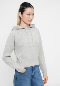 Grauer Kapuzenpullover aus gestricktem Material mit einem gerippten Saum, ausgestattet mit einer Kordelzugkapuze und langen Ärmeln, kombiniert mit hoch taillierten blauen Jeans.