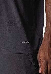 Černé tričko vyrobené z hladké tkaniny, s bílým logem ClimaCool poblíž lemu. Tričko má krátké rukávy a rovný střih.