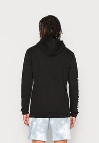 Sort hoodie med k�ängurulomme og justerbar hætte. Har hvidt logo-tekst på venstre ærme. Bæres med lyseblå tie-dye shorts.