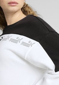 Puma särk, millel on must-valge värvi plokkdisain, pehme riie, ribaga ümar kaelus ja trükitud logo detailid rinna piirkonnas.