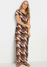 Robe maxi dans un motif tie-dye marron, avec un décolleté en scoop et des manches courtes. Fabriquée en tissu doux et extensible. Associée à des sandales noires.