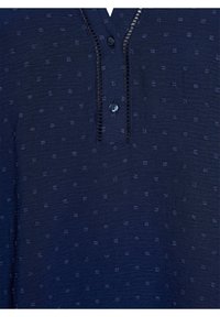 Camicia blu navy con un motivo testurizzato di piccoli punti, collo a V e una patta con due bottoni neri. Tessuto morbido.