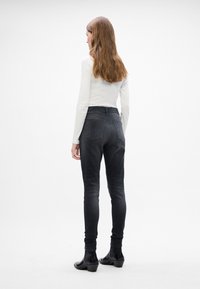 Fekete farmernadrág slim fit szabással, közepes magasságú derékkal és öt zsebes dizájnnal, fehér hosszú ujjú felsővel és bokacsizmával párosítva.