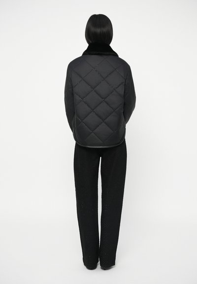 Μαύρο επενδυμένο μπουφάν με γιακά από συνθετική γούνα, με διαμαντένιο σχέδιο και ελαφρώς εφαρμοστό σχέδιο, συνδυασμένο με μαύρα υφασμάτινα παντελόνια.