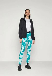 Melnā vieglā jaka, balts T-krekls un akva legingi ar abstraktiem ģeometriskiem rakstiem. Melnas sporta kurpes pabeidz apģērbu.