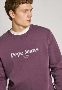Paarse sweatshirt van zacht materiaal met een ronde hals en witte logo-tekst "Pepe Jeans" met aanvullende locatiegegevens van Londen.