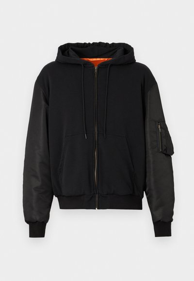 Μαύρο φούτερ με φερμουάρ, με λείο ύφασμα στο σώμα και μανίκια που μοιάζουν με σατέν. Διαθέτει εμπρόσθια τσέπη και επιπλέον τσέπη με φερμουάρ στο μανίκι.