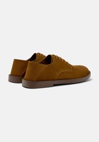 Scarpe in suede marrone con profilo basso e punta arrotondata. Presentano una chiusura con lacci e una suola in gomma marrone a contrasto.
