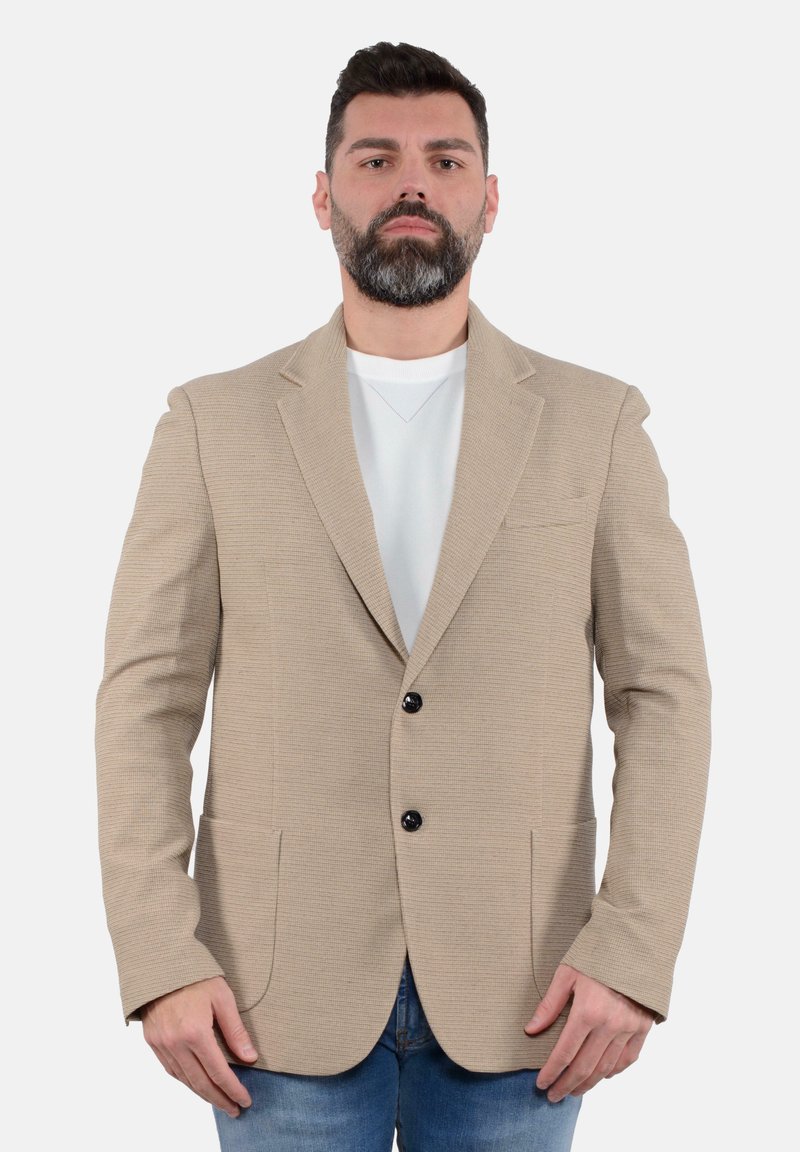 Blazer beige con texture, due tasche frontali, chiusura a un bottone e revers a scollatura profonda, indossato sopra una camicia bianca e jeans blu.