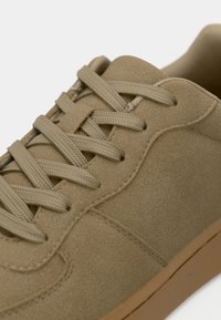 Κοντινό πλάνο σε ταμπά σουέντ αθλητικό παπούτσι με στρογγυλά κορδόνια στο ίδιο χρώμα, λεπτομερή ραφές και σόλα από καουτσούκ gum σε λευκό φόντο.