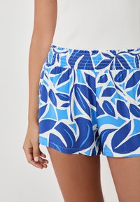 Shorts bleus à motif avec un design floral blanc, dotés d'une taille élastique et d'un tissu léger, atteignant le mi-thigh.