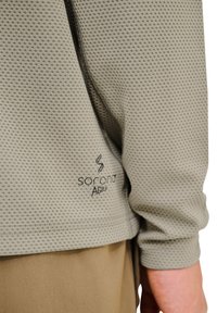 Hellgraues, strukturiertes Langarm-Oberteil mit einem Wabenmuster und dem Logo "Sorona Agile" an der Taille. Weicher Stoff, lockere Passform und runder Saum.