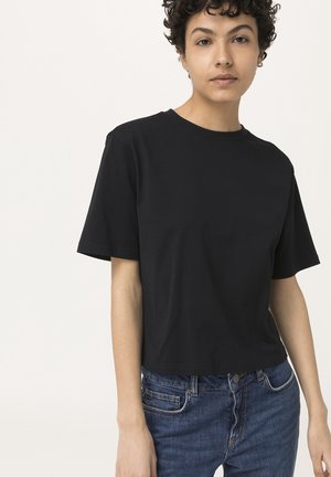 Camiseta de algodón negra con mangas cortas y cuello redondo, con un corte relajado y una textura suave. Combinada con jeans de mezclilla azul.